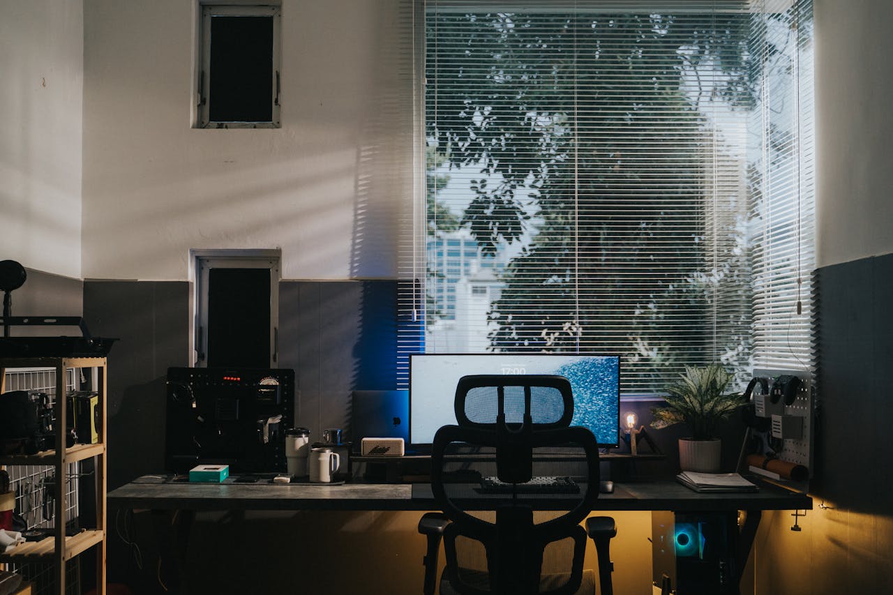 Cozy office workspace featuring desk, monitor, chair, and natural lighting through blinds.