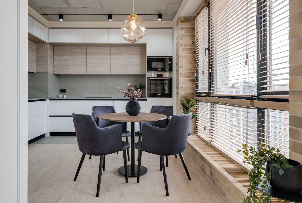 Spacious minimalist kitchen with round table and elegant chairs by large windows, perfect for bright spaces.